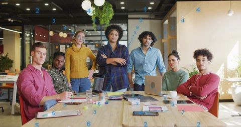 Diverse creative team collaborating around wooden table in modern office with laptops