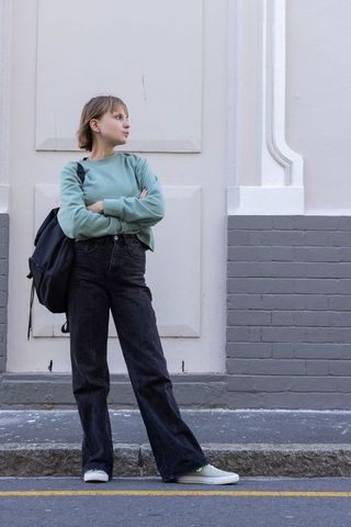 Young woman standing on curb looking sideways wearing mint sweatshirt and black backpack