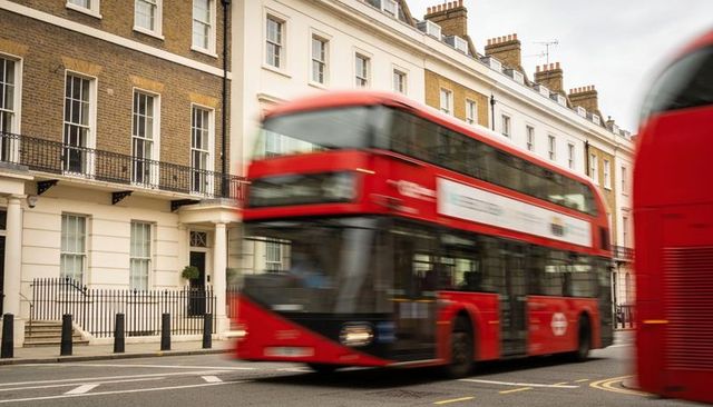 Motion-blurred red double-decker bus speeding past terraced houses along london street