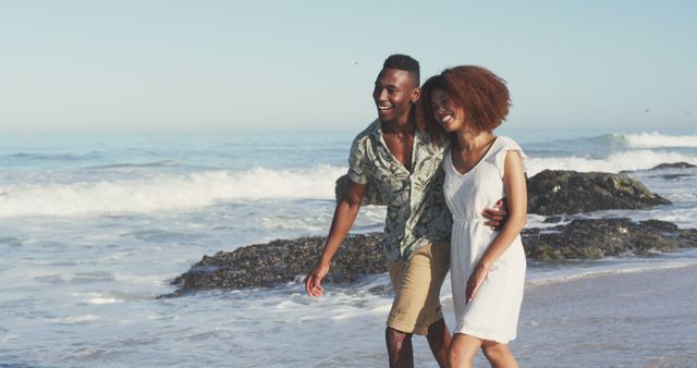 Happy diverse couple embracing and walking on sunny beach by the sea. Summer, free time, relaxation, romance and vacations.