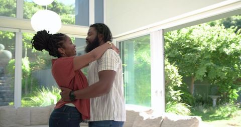 African american couple embracing in sunlit modern living room with garden view