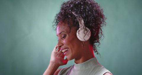 Joyful African American woman listening to music with white headphones and hoop earring