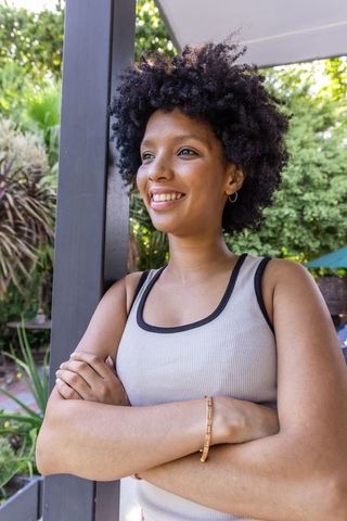Sunlit african american woman standing confidently on patio leaning on pergola post