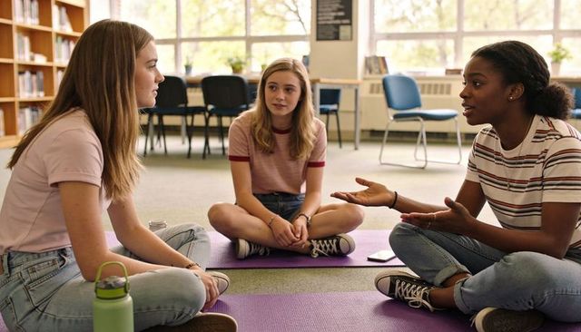 Teen students sitting in circle listening and discussing on purple mats in school library
