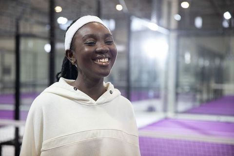 Smiling african american woman in white hoodie and terry headband on purple padel court