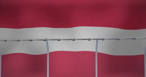 Perimeter security fence with razor wire showing against red white striped flag backdrop