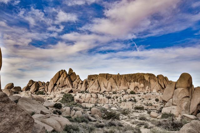 Desert landscape with large rocky formations and a blue sky filled with scattered clouds. The rugged terrain presents natural beauty, making it perfect for travel advertisements, adventure promotions, environmental presentations, and wallpaper backgrounds.