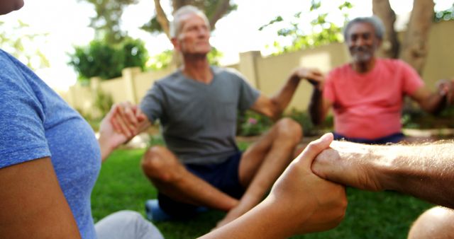 This image depicts a group of seniors in a garden, holding hands and meditating. The scene represents togetherness, relaxation, fitness and mental wellness in a peaceful outdoor environment. Ideal for use in articles, advertisements, and campaigns promoting senior activities, mental health and community engagement.