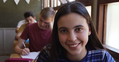 Smiling Teenage Girl in Classroom with Peers Studying Behind