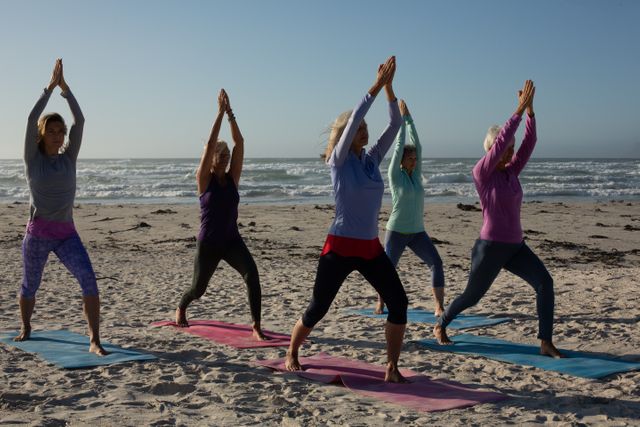Group of women practicing yoga on a beach at sunrise, standing in a yoga position. Ideal for promoting fitness, wellness retreats, outdoor activities, and healthy lifestyle content. Perfect for use in advertisements, social media posts, and wellness blogs.