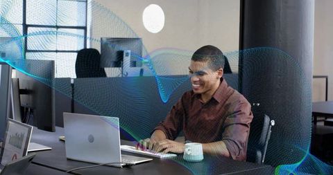 Smiling professional typing on laptop in open office, teal digital wave overlay