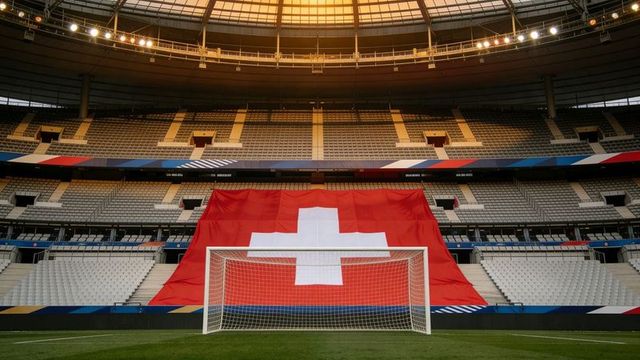Swiss flag draping behind soccer goal in empty modern stadium under warm golden light