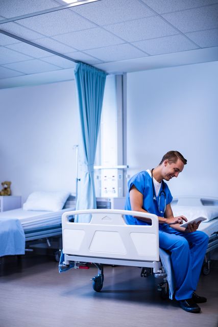 Doctor sitting on hospital bed and using digital tablet in ward of hospital