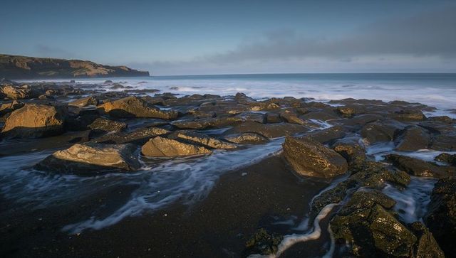 Rocky shoreline glistening in golden low sun with tide pools, seafoam and distant headland