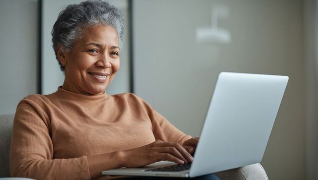 Senior woman typing on laptop at home, smiling and working remotely in cozy living room