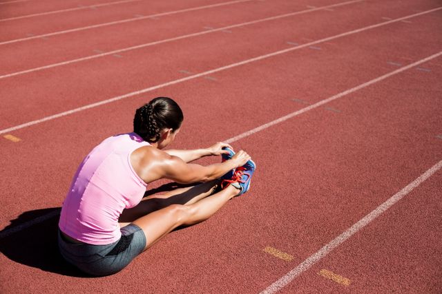 Female athlete stretching her hamstring on a running track. Ideal for use in fitness blogs, sports training guides, health and wellness articles, and promotional materials for athletic gear or sports events.