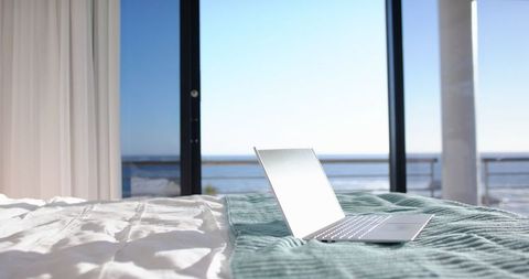 Stylish laptop overlooking ocean in modern coastal bedroom