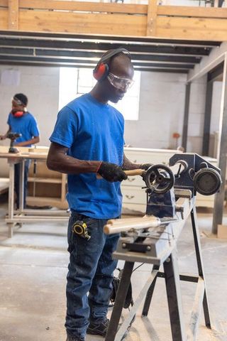 Woodworker shaping wooden spindle on lathe in carpentry workshop with safety gear