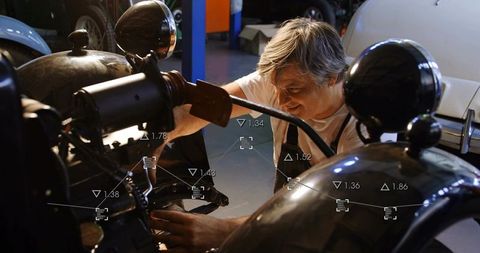 Silver-haired mechanic repairing vintage motorcycle engine with diagnostic overlay