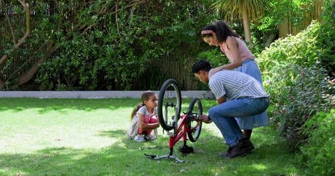 Father and Daughters Repairing Bicycle in Backyard