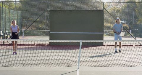 Mixed-gender tennis players practicing on public hardcourt with backboard and net in park