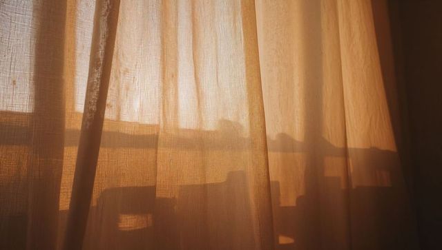 Golden Sunlight Filtering Through Sheer Curtain Casting Balcony Rail and Chair Silhouettes