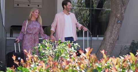 Happy couple departing hotel with luggage on sunny day