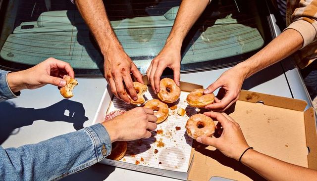 Reaching hands grabbing glazed donuts from cardboard box on car rear deck