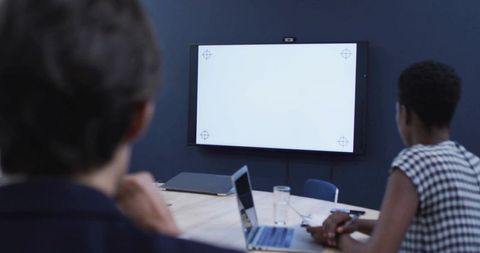 Leaning Black woman taking notes during corporate meeting with laptop and blank display