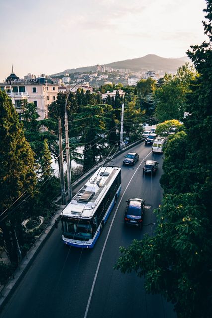 Urban road winding through mountainous city with a trolleybus and mixed traffic. Ideal for concepts related to transportation, city infrastructure, travel, and commuting. Can be used for travel blogs, urban development articles, and transportation publications.