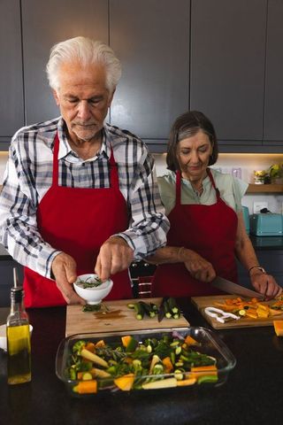 Senior couple enjoying cooking and slicing vegetables in modern kitchen