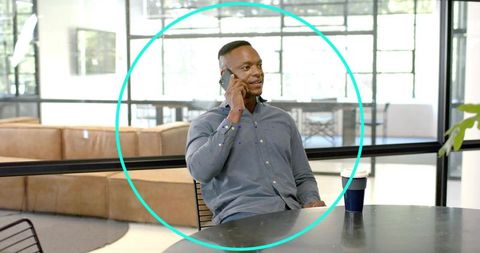 Businessman talking on smartphone at modern glass-walled office lounge holding coffee cup