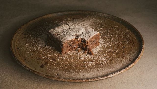 Bitten chocolate brownie sitting on rustic ceramic plate revealing gooey center, powdered sugar