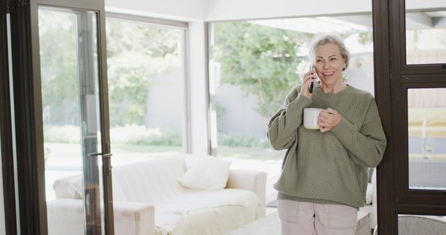 Happy Mature Woman Talking on Phone While Holding Coffee Cup in Bright Living Room - Download Free Stock Images Pikwizard.com