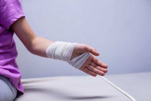 This image shows a young girl with a bandaged hand sitting on a hospital bed. It can be used in healthcare and medical contexts, such as articles about pediatric care, injury recovery, and hospital treatments. It is also suitable for educational materials on first aid and emergency response.