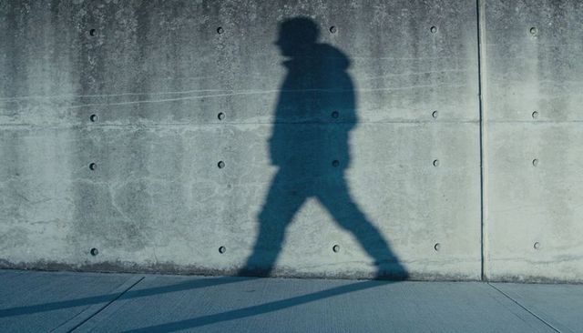 Walking Hooded Silhouette Casting Long Shadow on Textured Concrete Wall, Urban