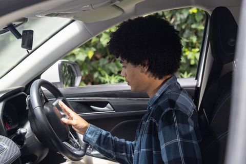 Young man sitting at wheel holding steering wheel and checking dashboard in parked car