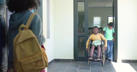 African american teen pushing wheelchair in school corridor with friend showing inclusion