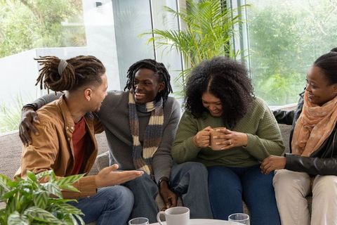 African american friends laughing and chatting on sofa during cozy coffee and conversation
