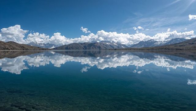 Mirroring alpine lake reflecting blue sky, cumulus clouds and snow-capped mountains