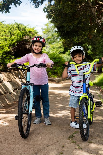 Portrait of smiling children standing with bicycle in park on a sunny day