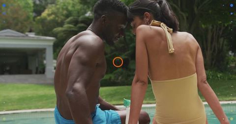 Sunlit couple leaning by backyard pool sharing tropical drink, summer swimwear intimacy