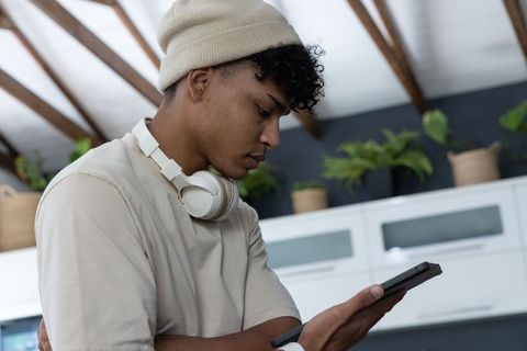 African american man checking phone in modern kitchen with headphones and beanie