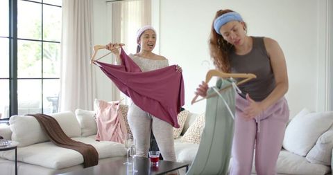 African american friends comparing outfits at home holding garments on wooden hangers