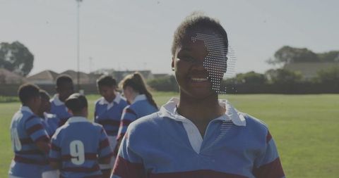 Teen rugby player smiling on field while team huddling and coach calling play