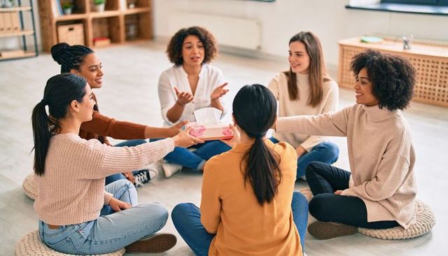 Women sitting in support circle sharing feelings, passing tissues during group discussion