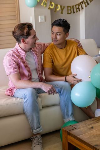 Celebrating birthday at home male partners embracing with teal and white balloons