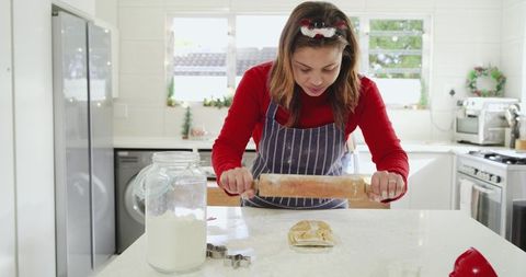 Woman rolling dough with wooden rolling pin for holiday baking in sunlit kitchen