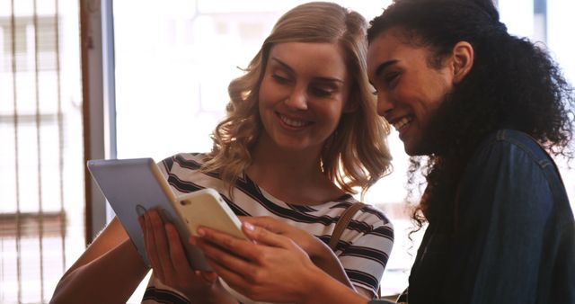 Two Women Smiling and Sharing Content Using Digital Devices - Download Free Stock Images Pikwizard.com