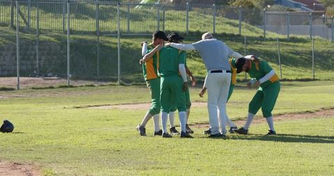 Youth baseball team huddling with coach on sunny community field in green uniforms